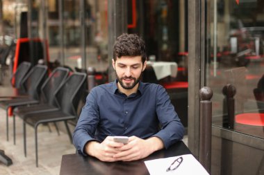 Kafeterya masada oturan ve yanında smartphone ile sohbet mutlu adam