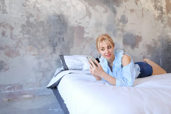Чарівна жінка тримається в руках і використовує смартфон, лежить на великому — стокове фото