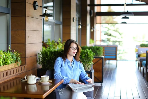 Ung kvinne leser aviser og bruker smarttelefon på restaurant – stockfoto