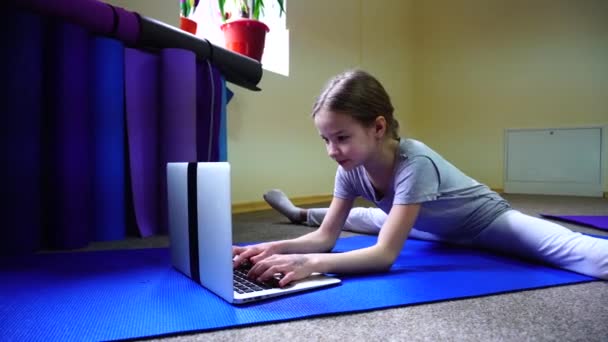 Girl sits on floor in twig position and rewritten with friend through internet on laptop. — Stock Video