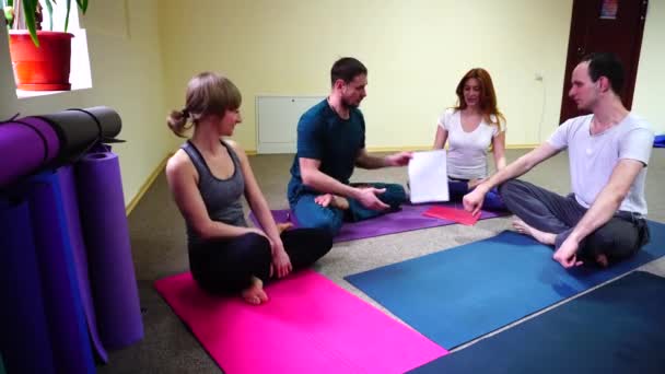 Четыре молодых человека сидят на полу на ковриках для йоги и общаются . — стоковое видео