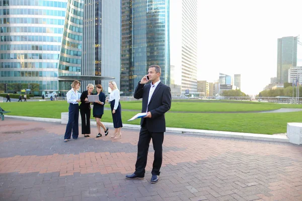 Businessperson talking by smartphone with employees in backgroun