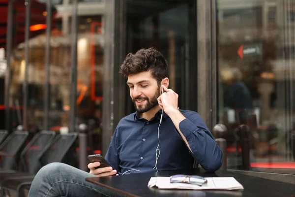 American boy listening to music at cafe with earphones and smart