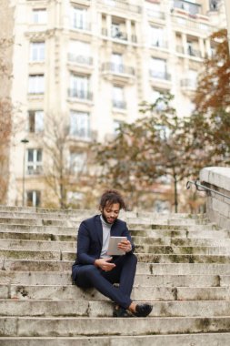 Tablet kullanma ve basamaklarında oturan melez işadamı.