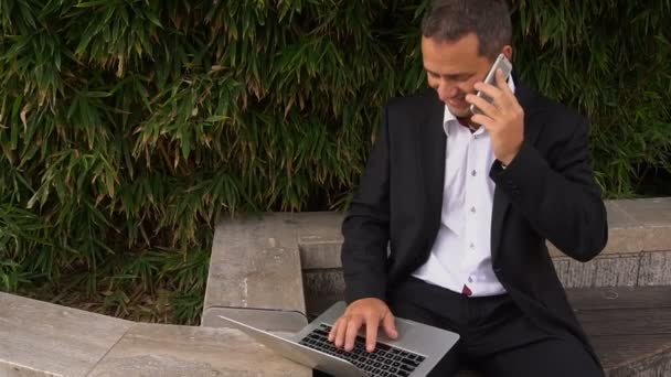Správce mluví o smartphone a práci s notebookem venku v pomalém pohybu. — Stock video