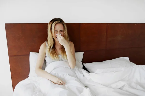 Боль девушка чихает в белой постели с салфеткой — стоковое фото