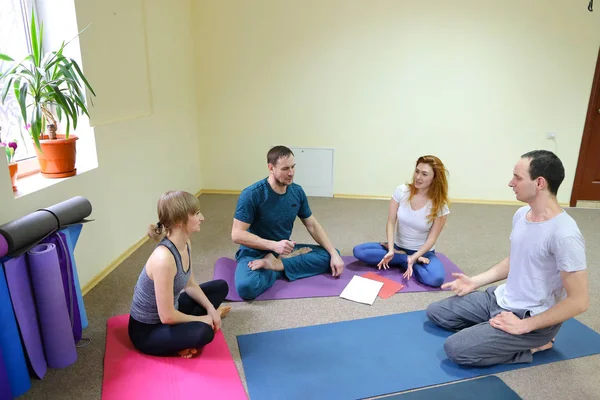 Two young women and two men sit on floor in fitness studio.