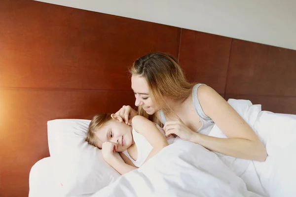 Beleza mãe acorda pequena filha na cama branca com luz do sol — Fotografia de Stock