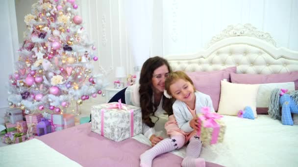 Hermosa mujer y niña, madre e hija en buen humor para jugar con los demás en el dormitorio brillante en la cama cerca del árbol de Navidad festivo . — Vídeos de Stock