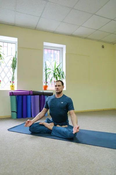 Handsome man sitting on floor on rug for yoga in lotus position