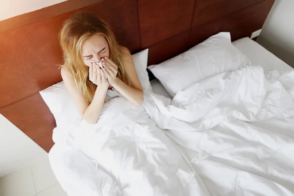 Девочка больна, чихает в белой кровати с салфеткой дома солнечный день — стоковое фото