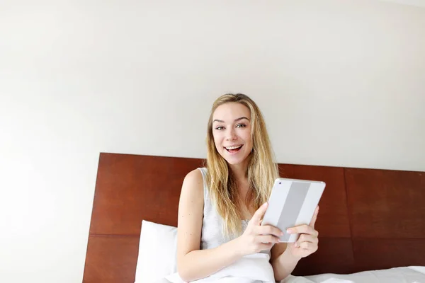 Portret super zadowolona młoda kobieta trzymać tabletkę o białe łóżko — Zdjęcie stockowe