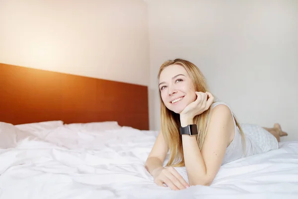 Retrato de la mujer advicing reloj electrónico inteligente en la mano, acostado en la cama blanca en el día soleado — Foto de Stock