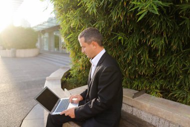 İşadamı çevre bitki dışarıda dizüstü bilgisayar ile çalışma  .