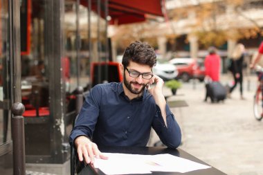 Smartphone tarafından savunarak ve kafe sekmesini kağıtları okuma işadamı