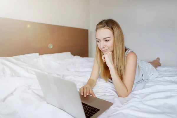 Mujer europea con el ordenador portátil trabajando en casa de forma remota en la cama blanca — Foto de Stock