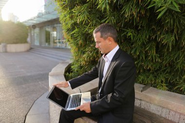 İşadamı çevre bitki dışarıda dizüstü bilgisayar ile çalışma  .