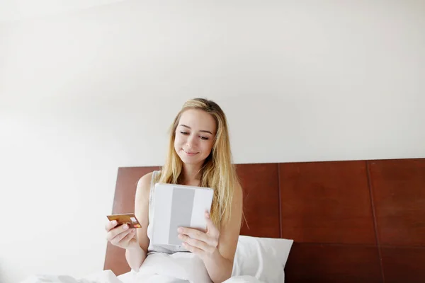 Csinál online bankárság nő tart betéti hitelkártyával és tabletta szóló fehér ágyban otthon a napsütés — Stock Fotó