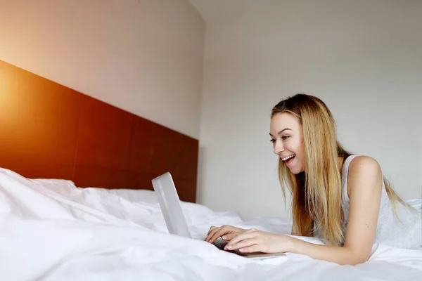 Mujer super feliz con el ordenador portátil trabajando en casa de forma remota en la cama blanca — Foto de Stock
