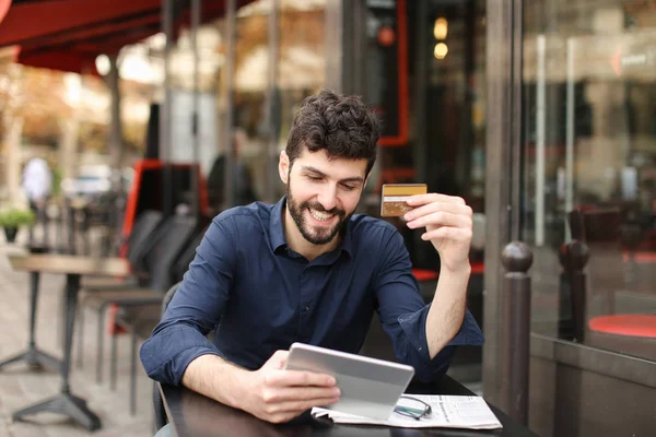 Happy man shopping online with card and tablet at street cafe wi