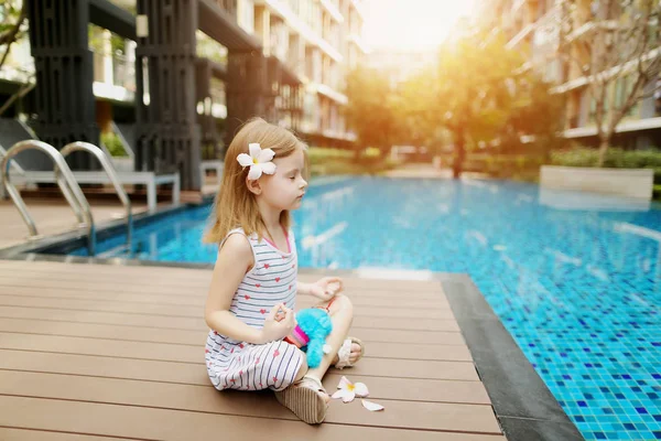 Niño pequeño haciendo ejercicios de yoga sentado cerca de la piscina con flores en un día soleado — Foto de Stock