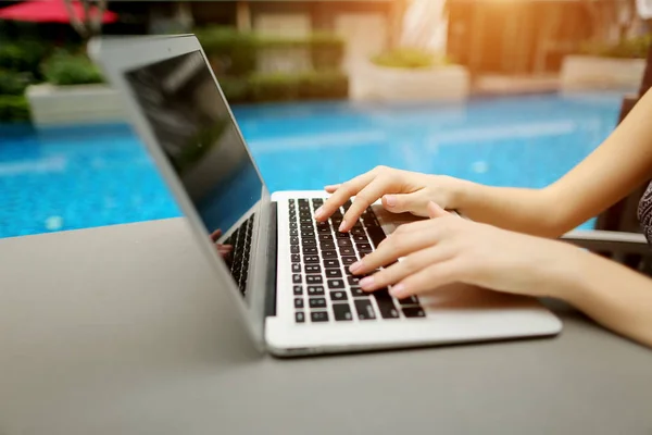 Cerrar las manos de la mujer presionando el teclado en el ordenador portátil día soleado piscina — Foto de Stock