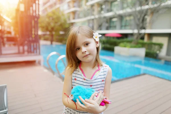 Lindo niño pequeño sosteniendo juguete en el fondo de la piscina y el edificio de apartamentos — Foto de Stock