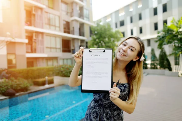 Mujer joven se ofrecen a firmar el documento de contrato en el fondo del nuevo edificio de apartamentos. Frente utilizado con licencia Open Font — Foto de Stock