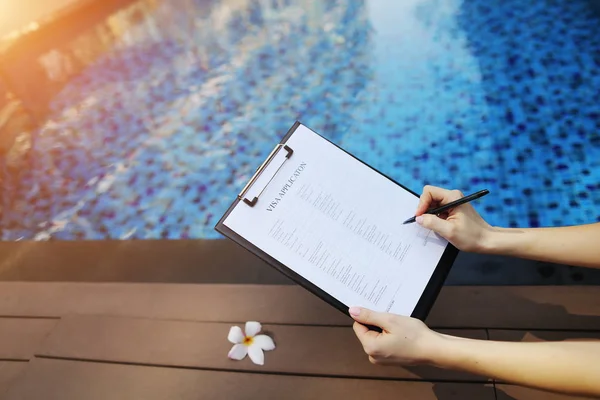 Primer plano de la mujer llena el formulario de solicitud de visado en Emiratos Árabes Unidos Dubai en el fondo de la piscina. Frente utilizado con licencia Open Font — Foto de Stock