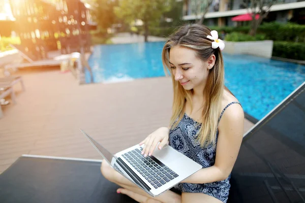 Mujer que trabaja utiliza Internet y PC portátil al aire libre de forma remota como freelancer cerca de la piscina y el edificio de apartamentos — Foto de Stock