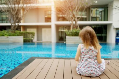 küçük geri güneşli günde Yüzme Havuzu yakın oturan çocuk