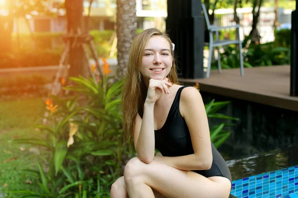 Mujer mirando a la cámara sonriendo cerca de la piscina en tailandiay mirando hacia arriba en día soleado — Foto de Stock