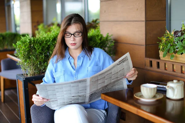 Mujer joven leyendo el periódico y utilizando el teléfono inteligente en el restaurante — Foto de Stock