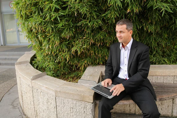 Businessman working with laptop outside near plant in  .