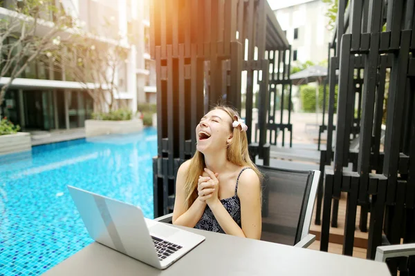 Joven hermosa chica es muy feliz Con el ordenador portátil cerca de la piscina en el día soleado . — Foto de Stock