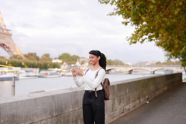 Young woman standing on embankment in Paris and watching photos