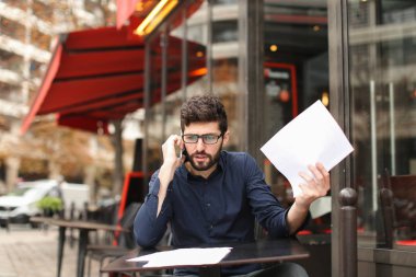 Smartphone tarafından savunarak ve kafe sekmesini kağıtları okuma işadamı