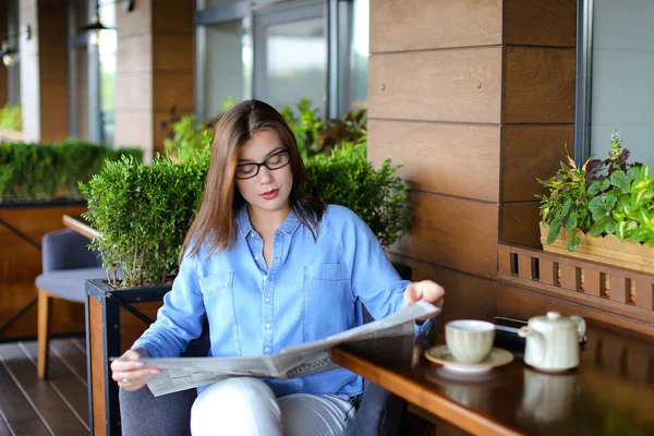 Pretty girl sitting at restaurant arm chair and reading newspape