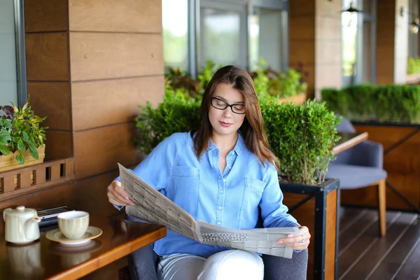 Young woman reading newspaper and using smartphone at restaurant