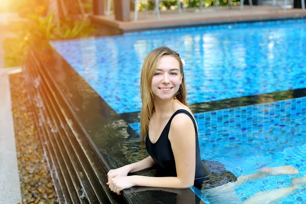 Mujer joven mirando la cámara disfrutar de la natación en la piscina azul al aire libre, relajarse cerca de las palmeras y el edificio de apartamentos en el país tropical — Foto de Stock