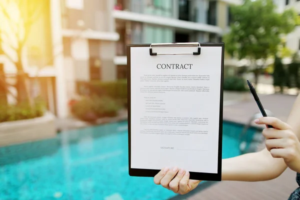 Primer plano de la mujer propone firmar el contrato en el contexto de un nuevo edificio con piscina. Frente utilizado con licencia Open Font — Foto de Stock