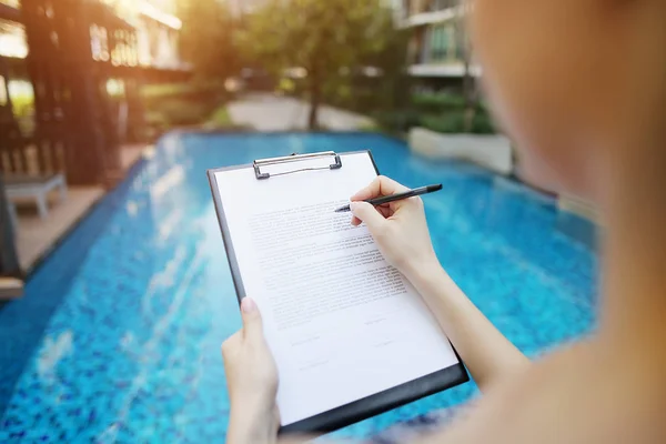 Chica firma papel contra el fondo de verano piscina de día soleado. Frente utilizado con licencia Open Font — Foto de Stock