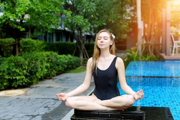 Mujer mentalmente fuerte sentada en posición de loto, haciendo yoga junto a la piscina en un día soleado — Foto de Stock