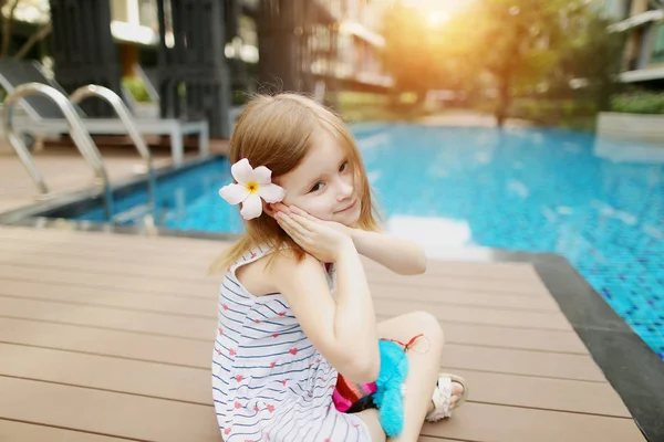 Lindo niño niña humana pequeña sentada cerca de la piscina con flores en el día soleado — Foto de Stock