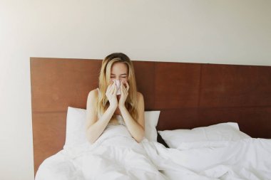 Sunlight sick Adult woman got cold, sneezes in white bed with napkin clipart