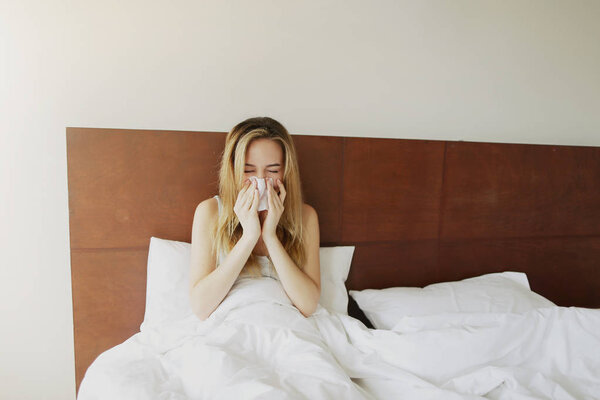 Sunlight sick Adult woman got cold, sneezes in white bed with napkin