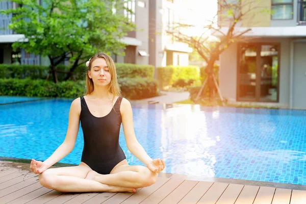 Retrato al atardecer de una mujer sentada en posición de loto, haciendo yoga junto a la piscina en un día soleado — Foto de Stock