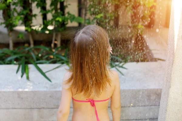 Portrait of drops of water fall on little girl back in swimsuit shower on sunny day outside — Stockfoto