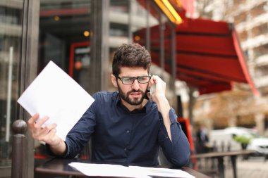 Smartphone tarafından savunarak ve kafe sekmesini kağıtları okuma işadamı