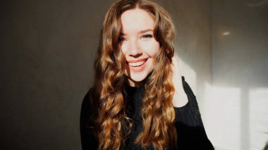 Genç kadın kıvırcık saçlı kameraya bakarak gülümseyen,